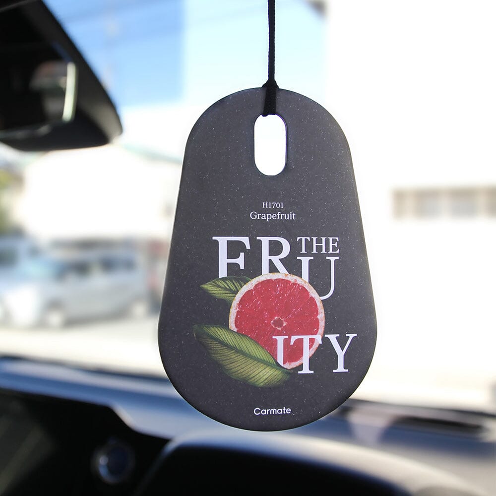 Car air freshener with grapefruit design hanging from a car's rearview mirror.