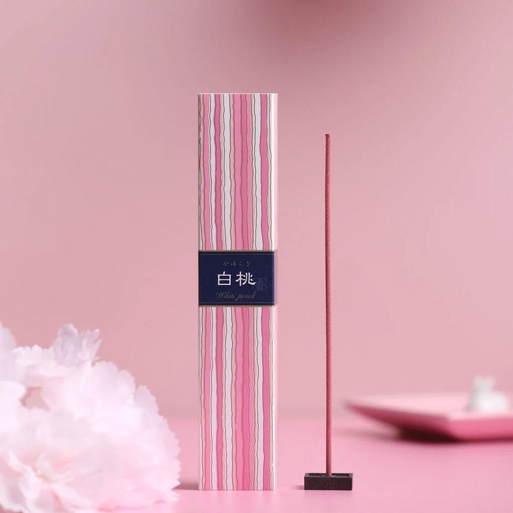 Kayuragi White Peach incense stick burning beside pink striped box on pink floral background