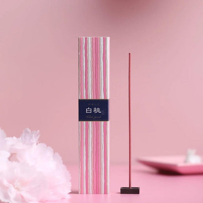 Kayuragi White Peach incense stick burning beside pink striped box on pink floral background